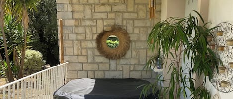 A patio with a table, chairs, a bench, a hanging light fixture, a decorative wall piece, and a potted plant.