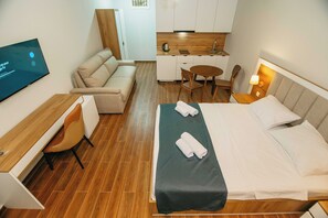 Habitación de hotel con cama, escritorio, silla, sofá, mesita pequeña y televisor.