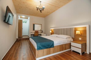 A bedroom with a wooden bed, a desk, a chair, a television, and a chandelier.