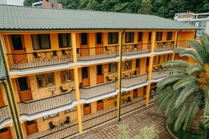 Un hotel de varios pisos con balcones, mesas al aire libre y una palmera.
