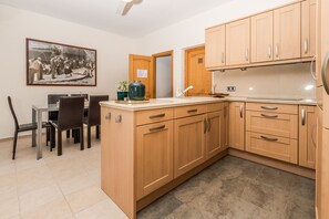 Une cuisine avec des meubles de rangement en bois, une table à manger avec des chaises et un tableau encadré au mur.