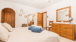 Ein Schlafzimmer mit einem Bett, einem Holzschrank, einem Spiegel und einem Deckenventilator.