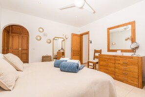 A bedroom with a bed, wooden wardrobe, a mirror, and a ceiling fan. - Villa Los Almendros (Javea)