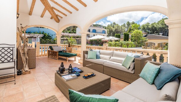 Ein überdachter Außenbereich mit Korbmöbeln, einem Esstisch und Blick auf die umliegende Landschaft.