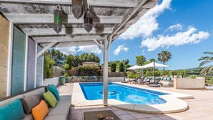 Ein überdachter Außenbereich mit Pool, Liegestühlen und einer Couch mit Kissen.