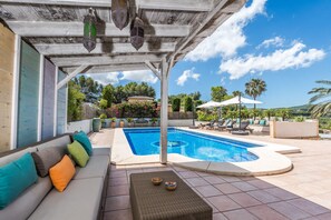 A covered outdoor area with a pool, lounge chairs, and a sofa with cushions. - Villa Los Almendros (Javea)
