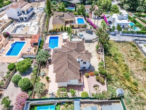 A residential area with multiple swimming pools, a large house with a tiled roof, and surrounding greenery. - Villa Los Almendros (Javea)