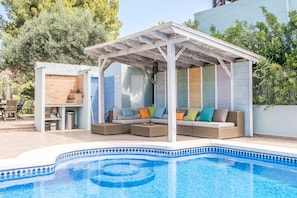 Ein Poolbereich mit überdachter Lounge, Grillplatz und einem gefliesten Pool.