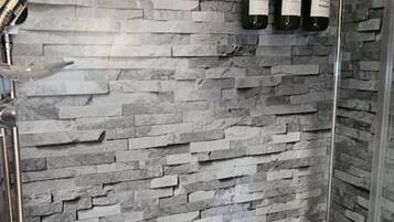 A shower with a stone wall, a glass door, and three bottles on the wall.