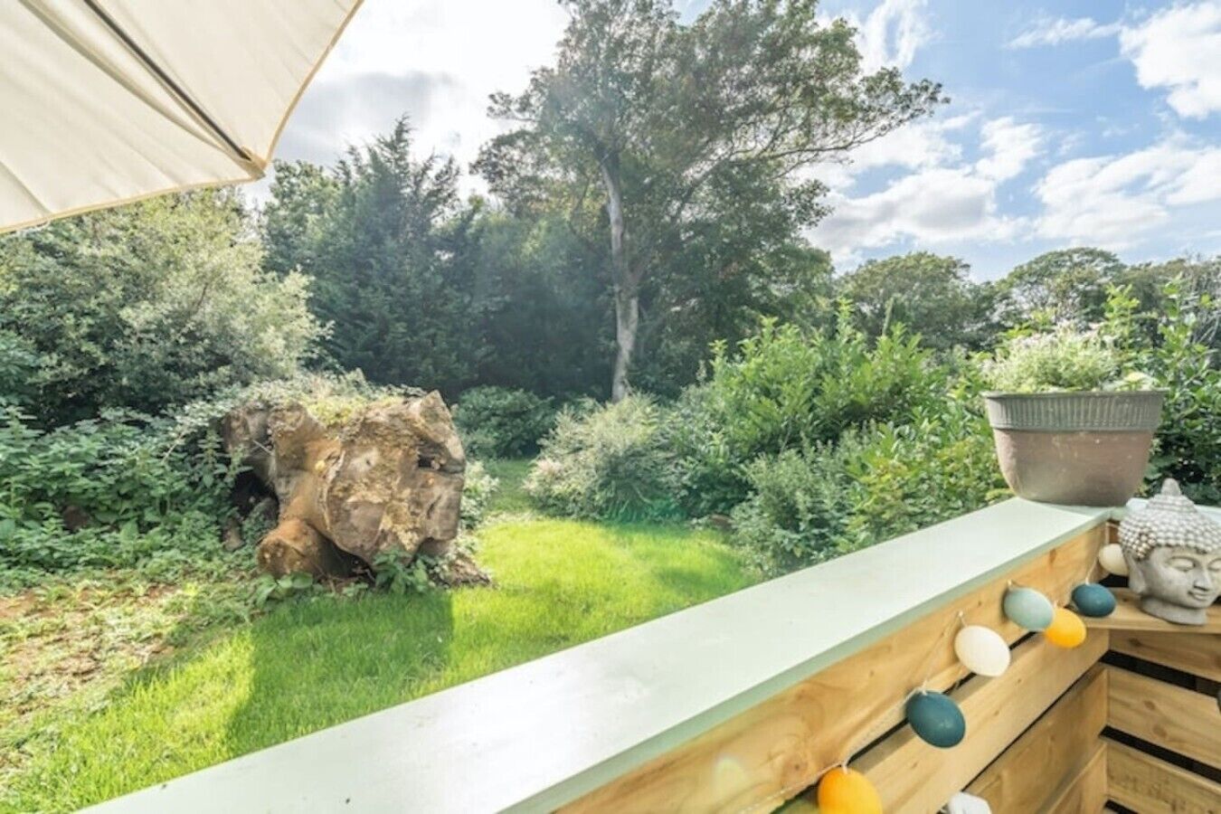 Een tuin met een houten bankje, een Boeddhabeeld en een bloempot.