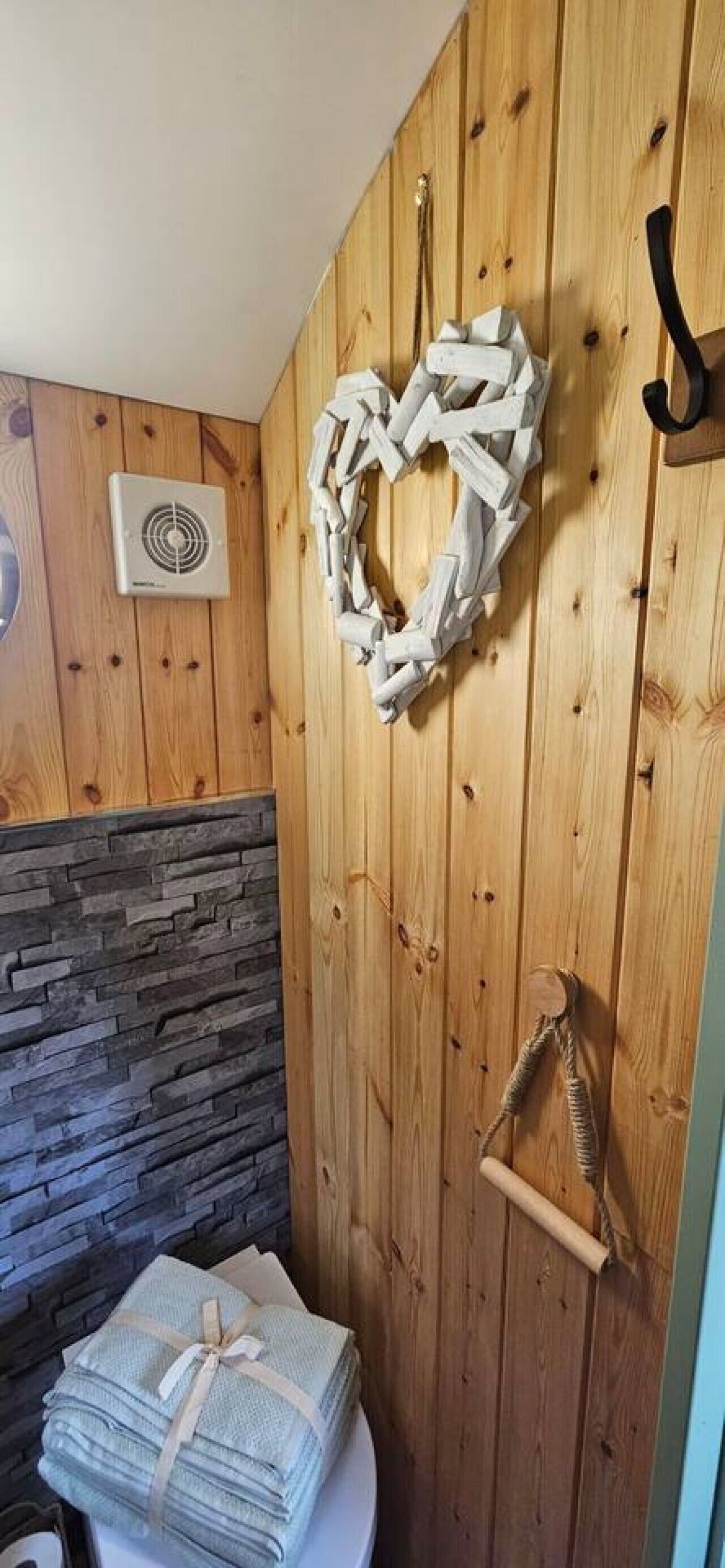 Une salle de bain avec des murs en bois, un mur d’accent en pierre, une décoration en forme de cœur, un porte-serviettes et un distributeur de serviettes.