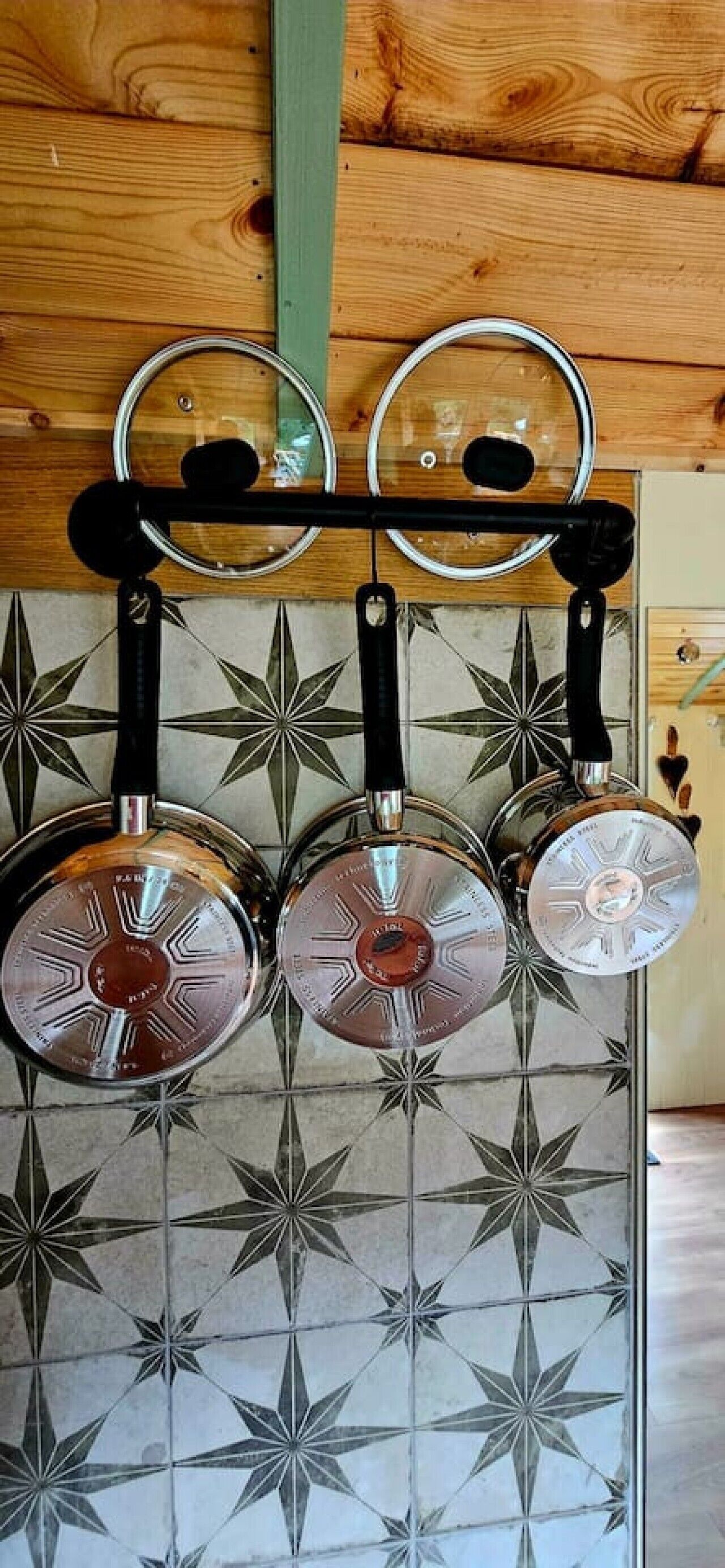 A kitchen with hanging pots on a rack, a wooden ceiling, and a tiled backsplash with a geometric pattern.