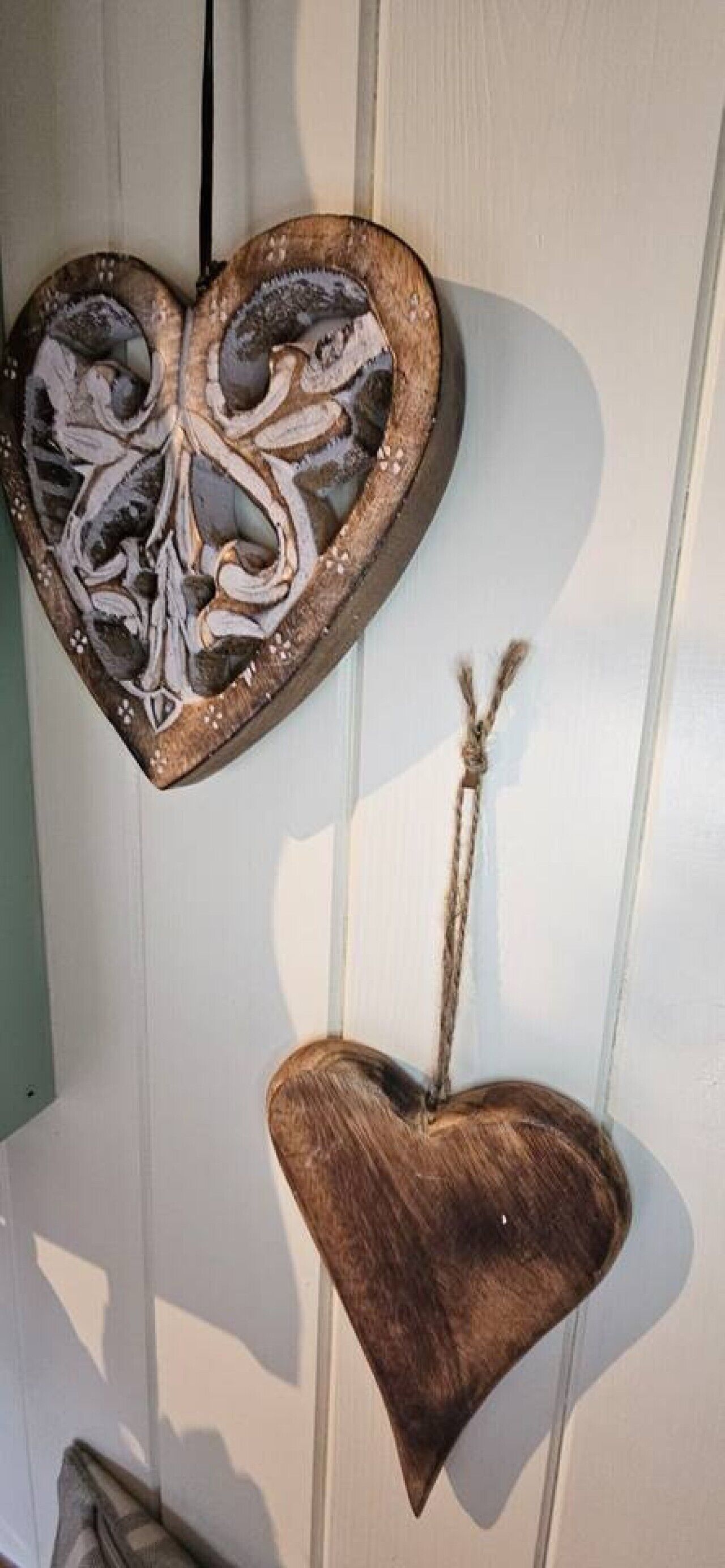 Dos adornos de madera con forma de corazón colgados en una pared blanca.