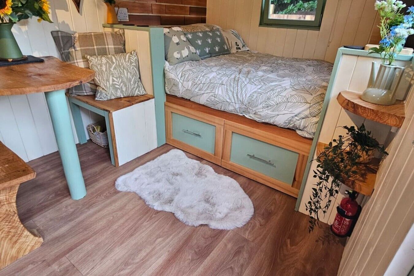 Una stanza accogliente con un letto, un tavolino, una panca e un tappeto morbido e bianco.