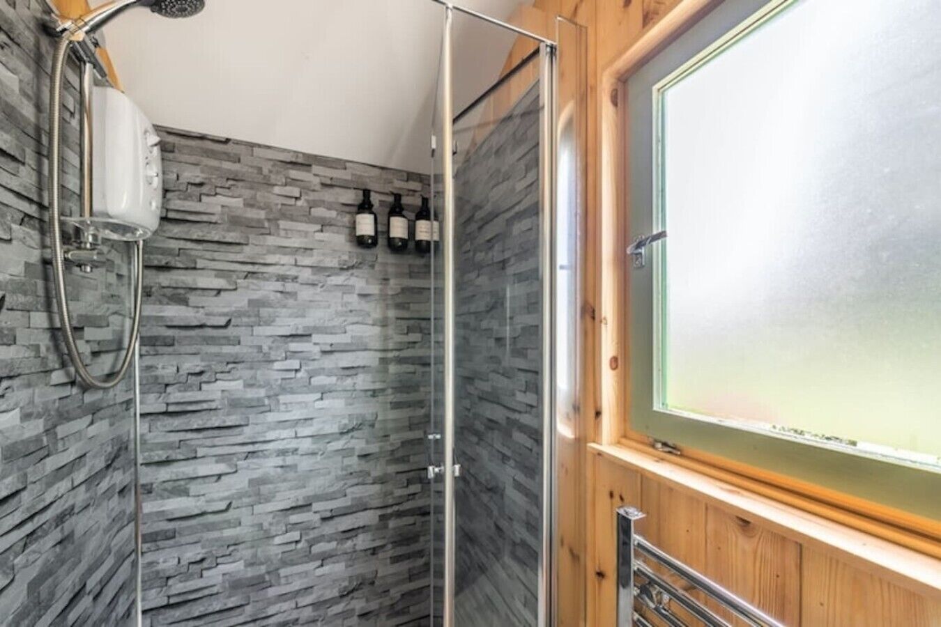 A shower with a stone wall, a wooden door, and a window with frosted glass.