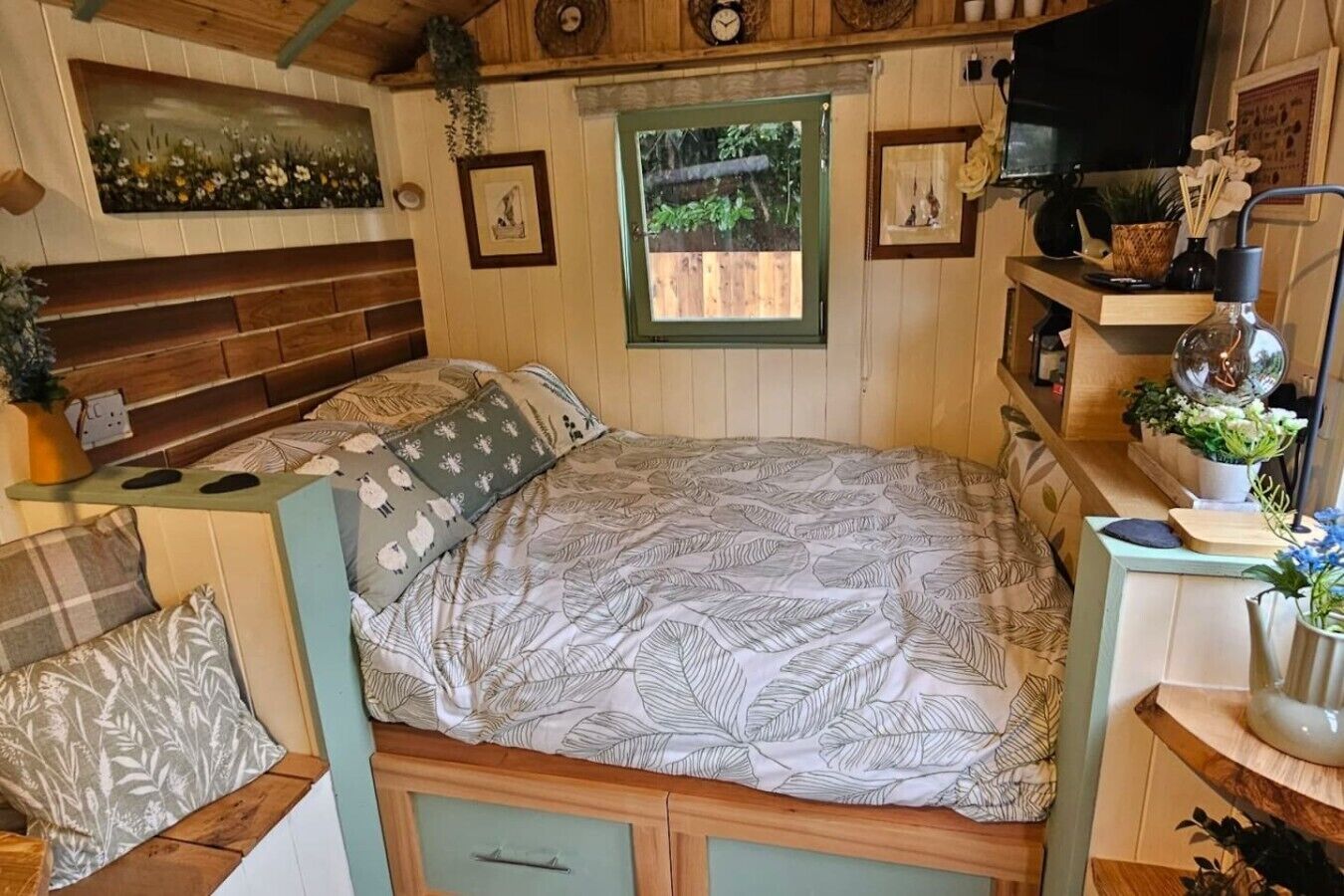 A cozy bedroom with a bed, a wooden headboard, a window, and a small desk with a plant.