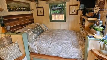 A cozy bedroom with a bed, a wooden headboard, a window, and a small desk with a plant.