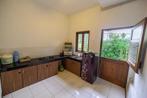 A kitchen with a gas stove, a refrigerator, a window with a view of greenery, and a sink. - Cozzy Villa Omah Nongko (yogyakarta)