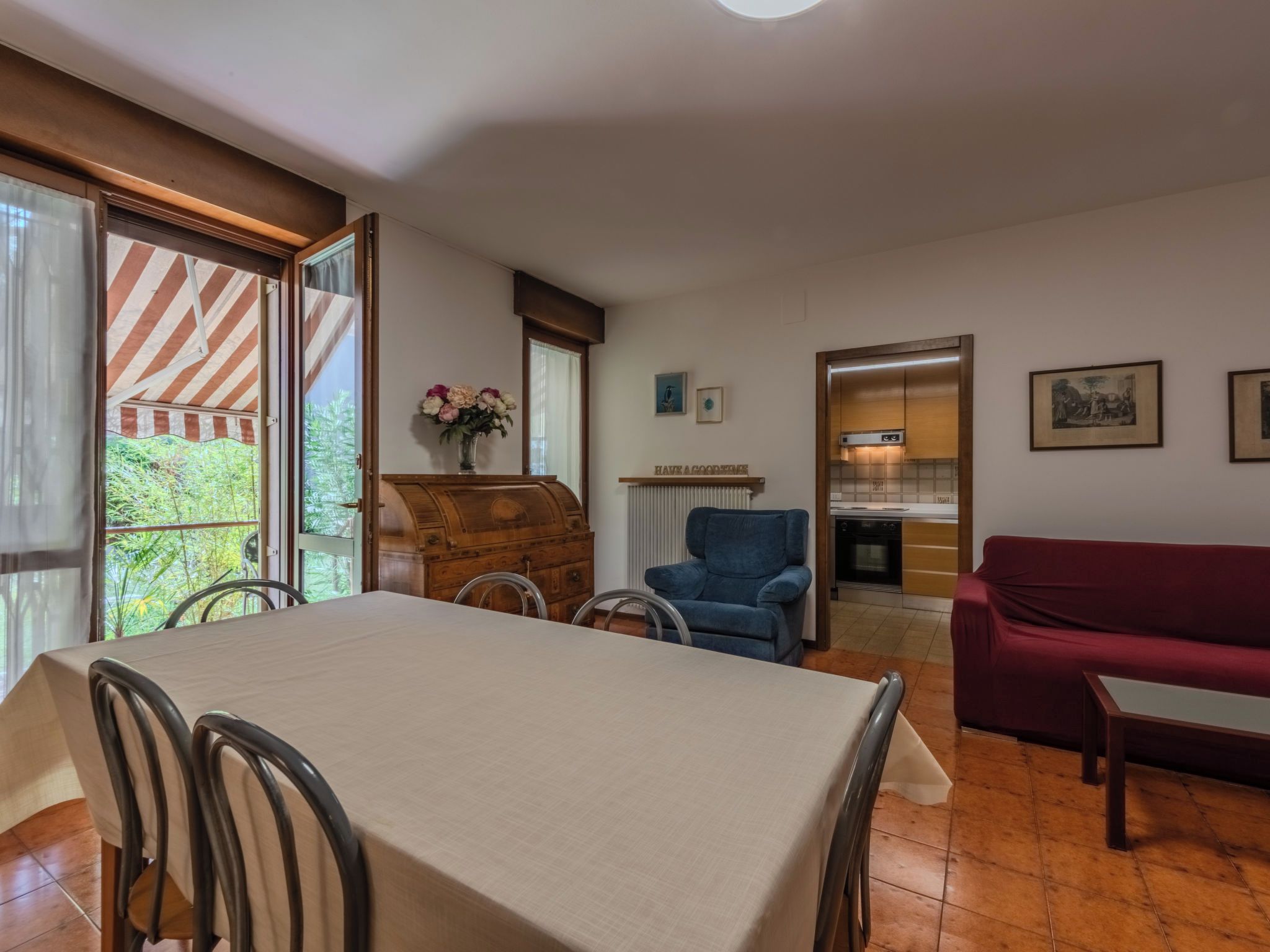 A dining area with a table and chairs, a blue armchair, a red sofa, and a kitchen in the background.