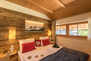 A wooden-paneled bedroom with a bed, red pillows, a mountain painting, and a window with a view. - Family-Friendly Apartment “Alpe Unterkehrhof” with Mountain View, Garden & Terrace (Lajen)