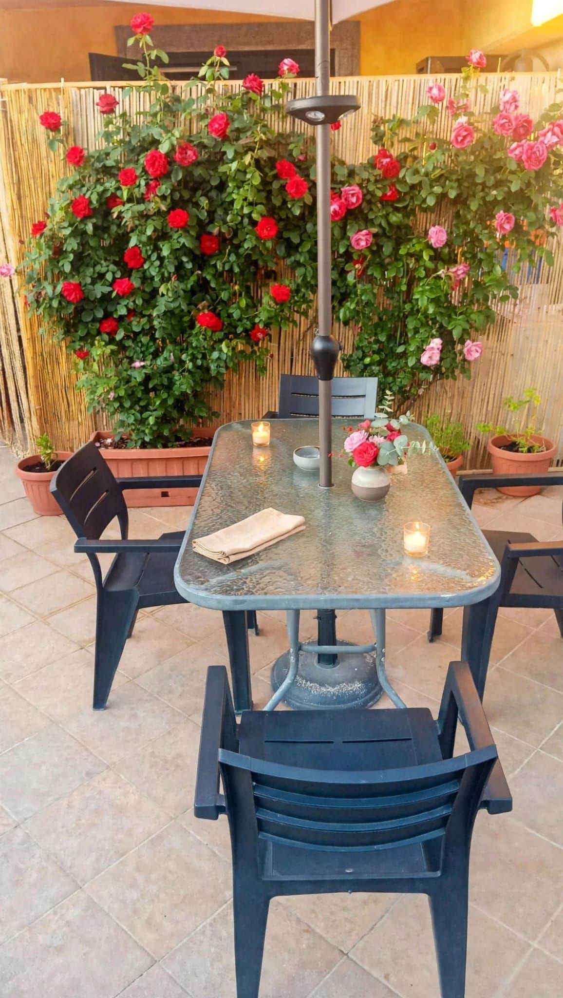 A glass-top table with chairs, a candle, and a vase with flowers.