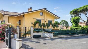 A yellow building with a gated entrance, a parking area, and a green fence.