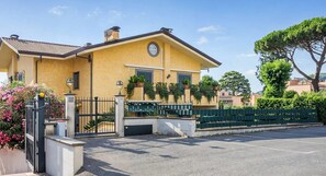A yellow building with a gated entrance, a parking area, and a green fence.