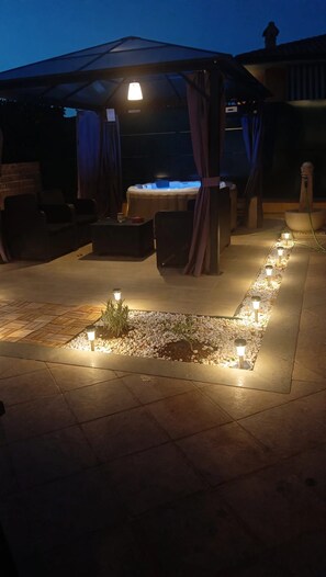 An outdoor patio area with a hot tub, seating, and decorative lighting.