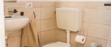 A bathroom with a toilet, bidet, sink, and a window above the toilet.