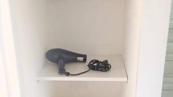 A bathroom with a toilet, a shelf with towels, a hairdryer, and toilet paper.