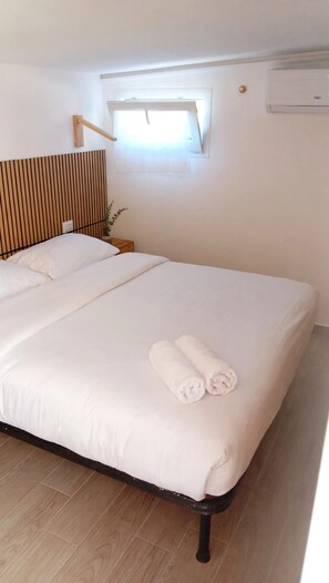 A hotel room with a bed, a window, an air conditioning unit, and a wooden headboard.