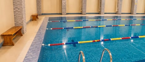 An indoor swimming pool with clear lane dividers, a wooden bench, and a stone pillar.