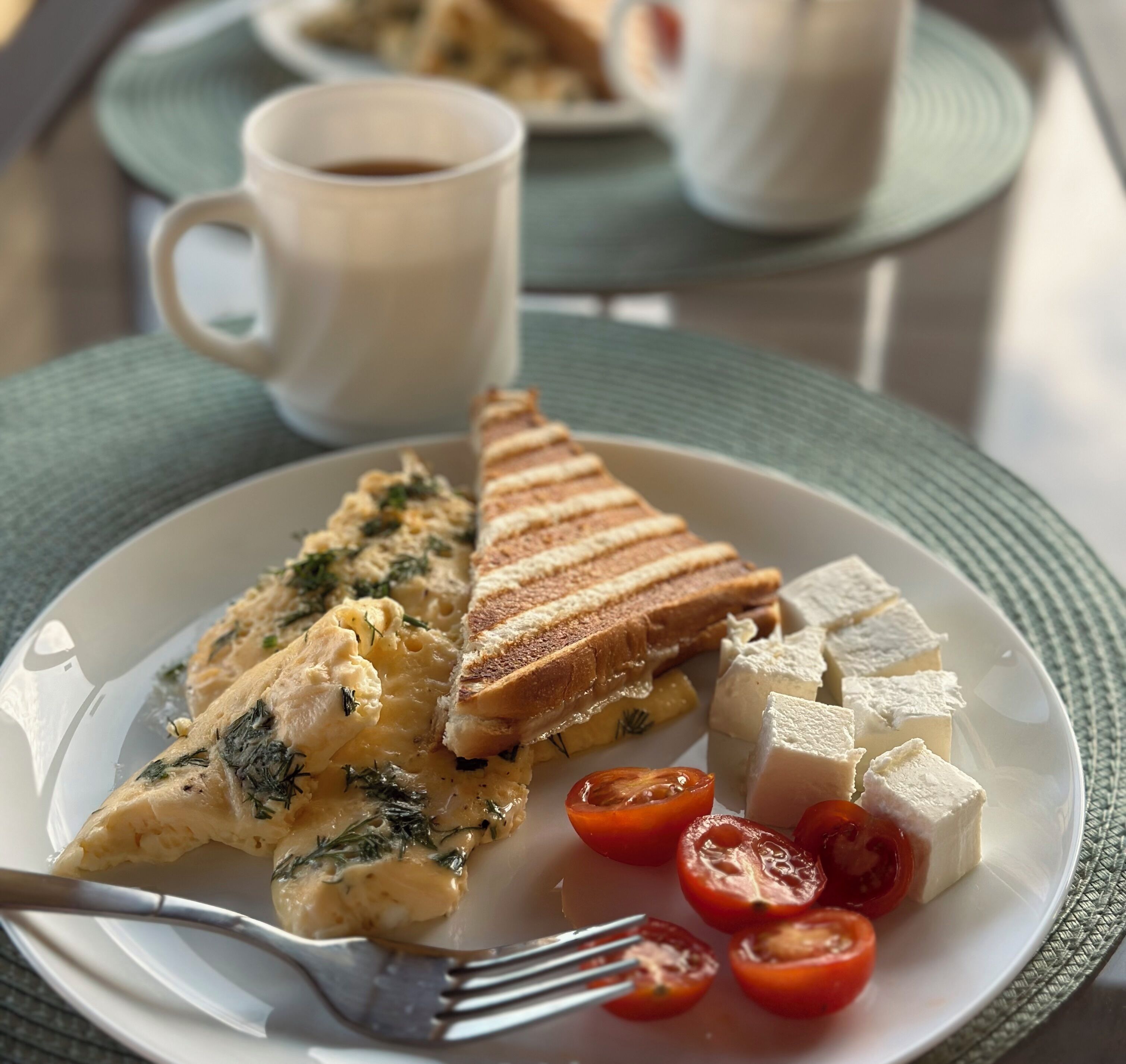 A plate with scrambled eggs, grilled cheese sandwich, cheese cubes, and cherry tomatoes.