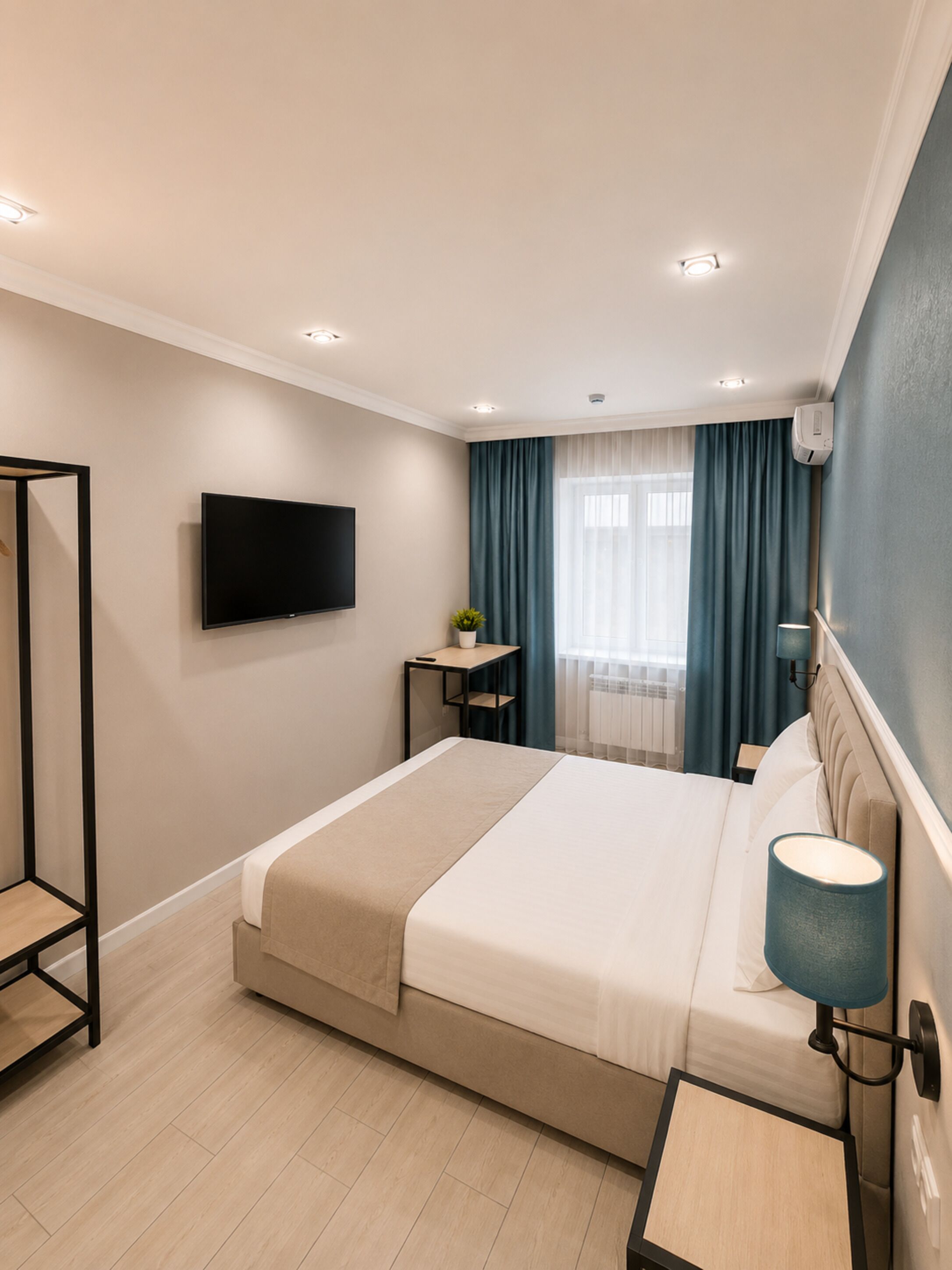 Moderni hotellihuone, jossa on sänky, televisio, yöpöytä, lamppu ja ikkuna, jossa on verhot.