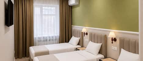 A hotel room with two beds, a television, an air conditioning unit, and a window with curtains.
