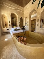 A room with a large bathtub, a bed, and a wooden door.