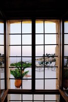 A window with a grid pattern, through which a patio area with chairs and a potted plant is visible.
