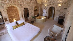 Una habitación con paredes de piedra, una cama, una bañera y un espacio para sentarse.