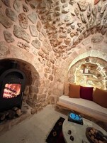 A stone-walled room with a fireplace, a sofa, and a table with a book and snacks.