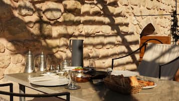 Une table dressée à l’extérieur, avec un mur de pierres en arrière-plan, agrémentée d’un pichet en métal, d’assiettes, de verres et de pain.