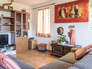 Ein Wohnzimmer mit einer Couch, einem Schrank mit Glastüren, einem Fernseher und einem Bild an der Wand.