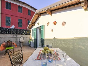 Eine Terrasse mit Esstisch, Stuhl, einem kleinen Tisch mit Obstschale und einer Karaffe.
