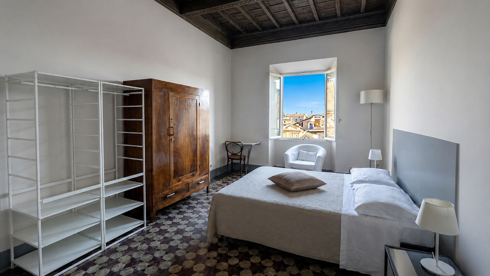 Une chambre à coucher avec un lit, une armoire, une chaise, une fenêtre donnant sur un beau paysage et une lampe.