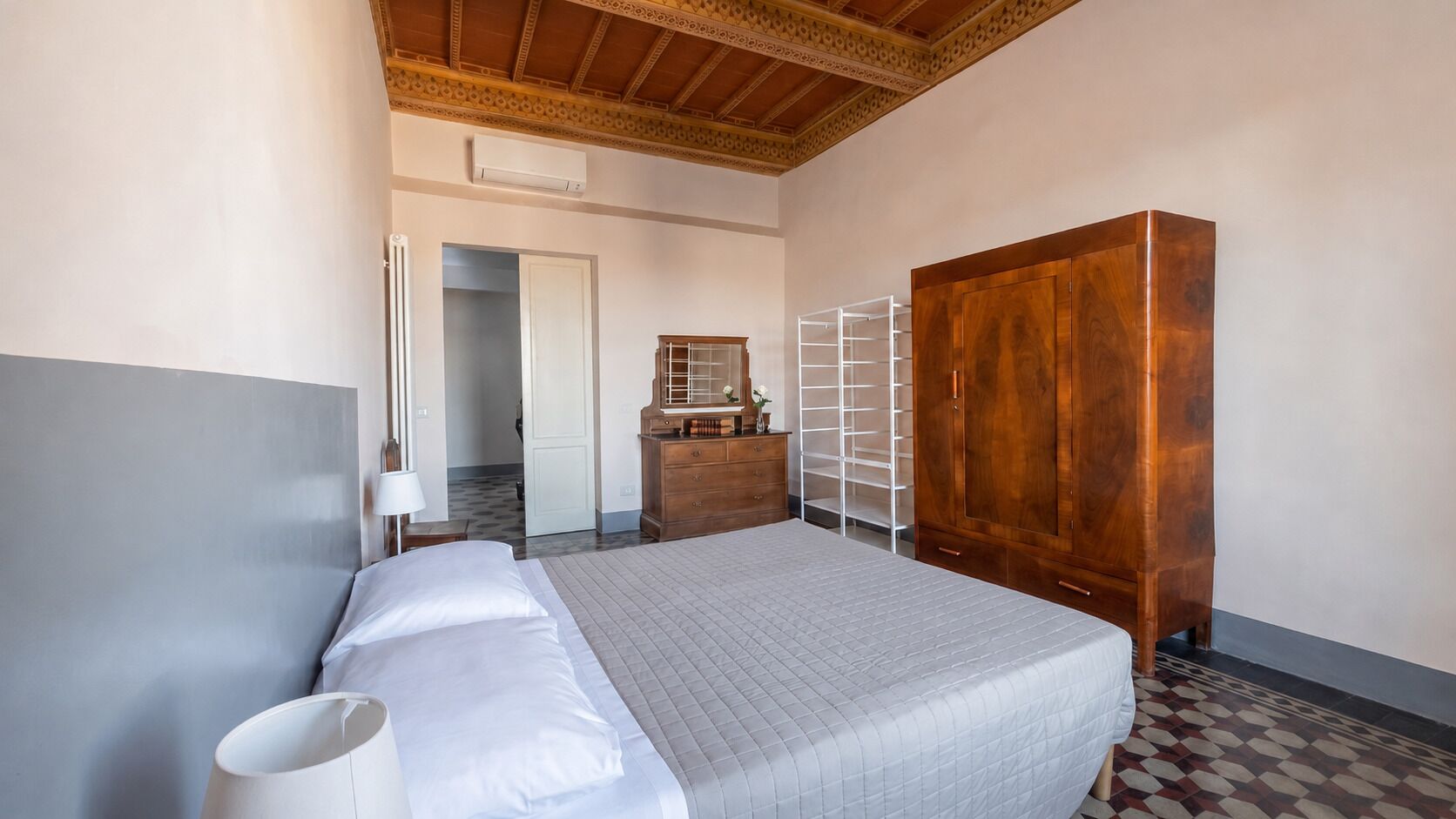 A hotel room with a bed, wardrobe, and a small desk with a lamp.