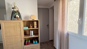 Huoneessa on rottinkikaappi, ikkunassa on verhot ja ovi johtaa toiseen huoneeseen.