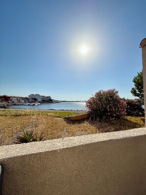 A coastal view with a clear sky, a boat, and a building in the background. - Les Roses by Alto Service (Le Barcarès)