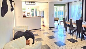 A spacious living area with a checkered floor, a dining table set for four, and a large window providing natural light. - Le Repos House—Sleeps 6—Pool—Pétanque (Alleins)