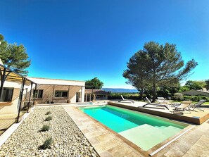 A modern pool area with a clear blue sky, a large tree, and a view of distant mountains. - Vrbo Property (Alleins)
