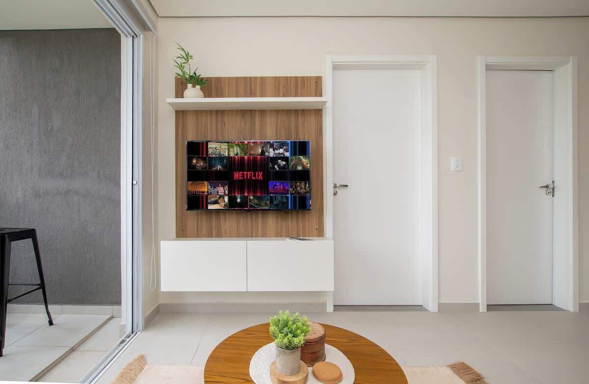 A modern living room with a flat-screen TV mounted on a wooden shelf, a small round table with a plant, and a sliding door.