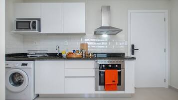 Eine kompakte Küche mit Waschmaschine, Mikrowelle, Backofen und einer Edelstahl-Dunstabzugshaube.